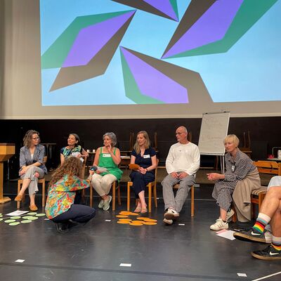 Moderatoren des Fachtags sitzen vor Leinwand bei Abschlussrunde