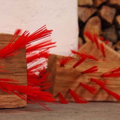 Marc Bertram, Titel der Skulptur: Scheit. Zu sehen sind Holzscheite in denen, wie bei einem Besen, rote Plastikfasern eingearbeitet sind.