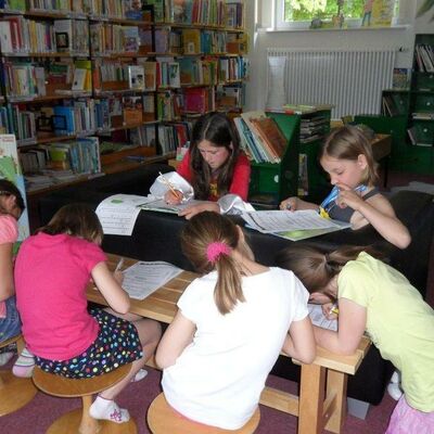 Auf deisem Bild sitzen 5 Schulkinder im Viereck an einem Tisch und lesen. Das Bild kommt aus der Kreisbücherei in Edemissen.