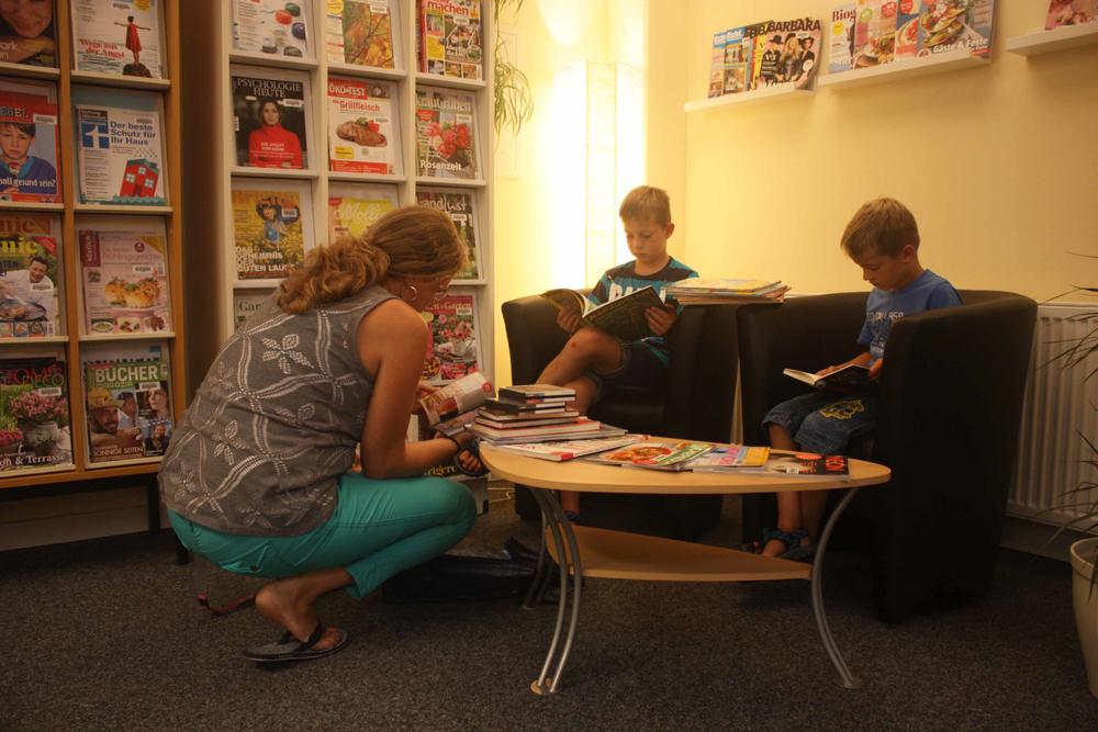 In der Kreisbücherei Wendeburg wird viel gelesen. Hier sind zwei Kinder und eine erwachsene Frau abgebildet.