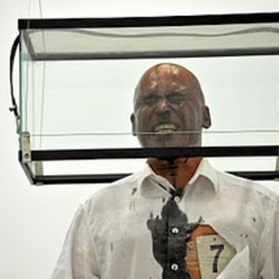 Dr. Helge Meyer, der Performancekünstler Helge Meyer steht mit Schmerzverzerrtem Gesicht in einem Glaskasten der über seinem Kopf schwebt.