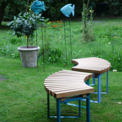 Diese gestaltete Gartenbank von Anne Christine Reetz ist geschwungen, hat blaue Füße und dunkles Eichenholz.