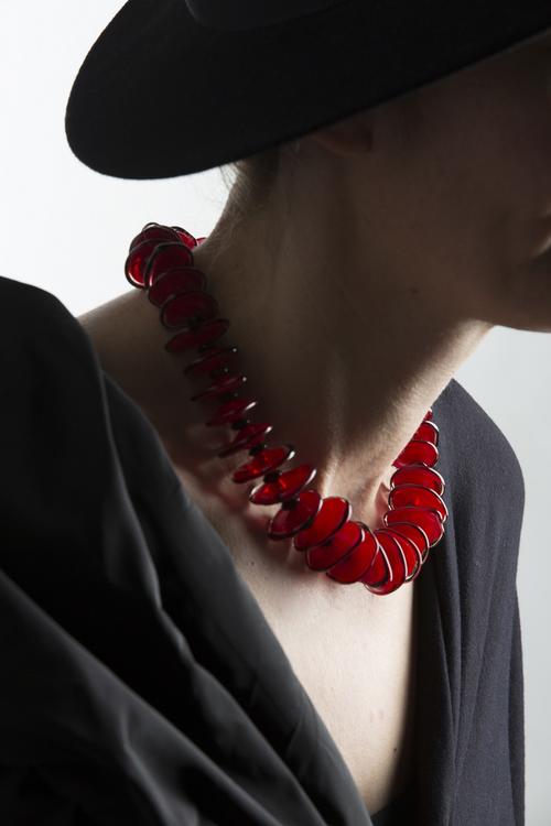Brigitte Scherzer stellte hier eine rote Halskette aus flachen roten Steinen her. Sie hängt an einem Hals einer Frau.