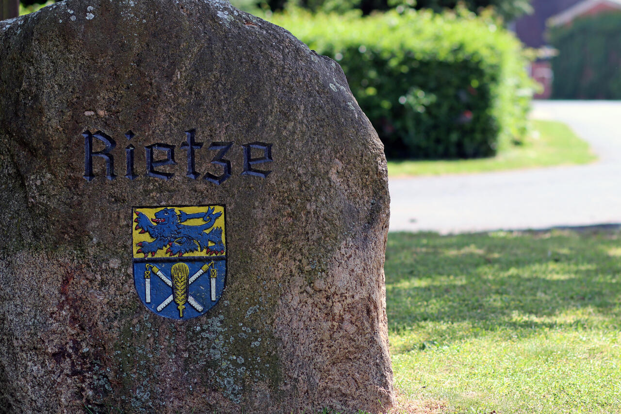 Auf einem Stein ist der Ortsname "Rietze" und das Wappen des Ortes eingraviert.
