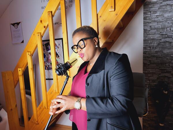 Die Sängerin Precious Refilwe steht vor einem Mikrofon und vor einer Treppe.