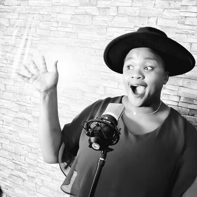 Die Sängerin Precious Refilwe steht vor einer Wand und singt in ein Mikrofon mit weit geöffnetem Mund.